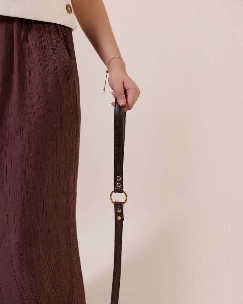 The bond dark brown vegetable tanned leather dog lead with solid zinc hardware held by a person in a brown skirt